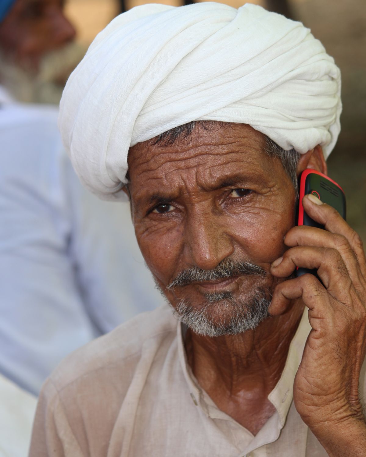 An elderly man in a white turban holding a feature phone to his ear, mid-call